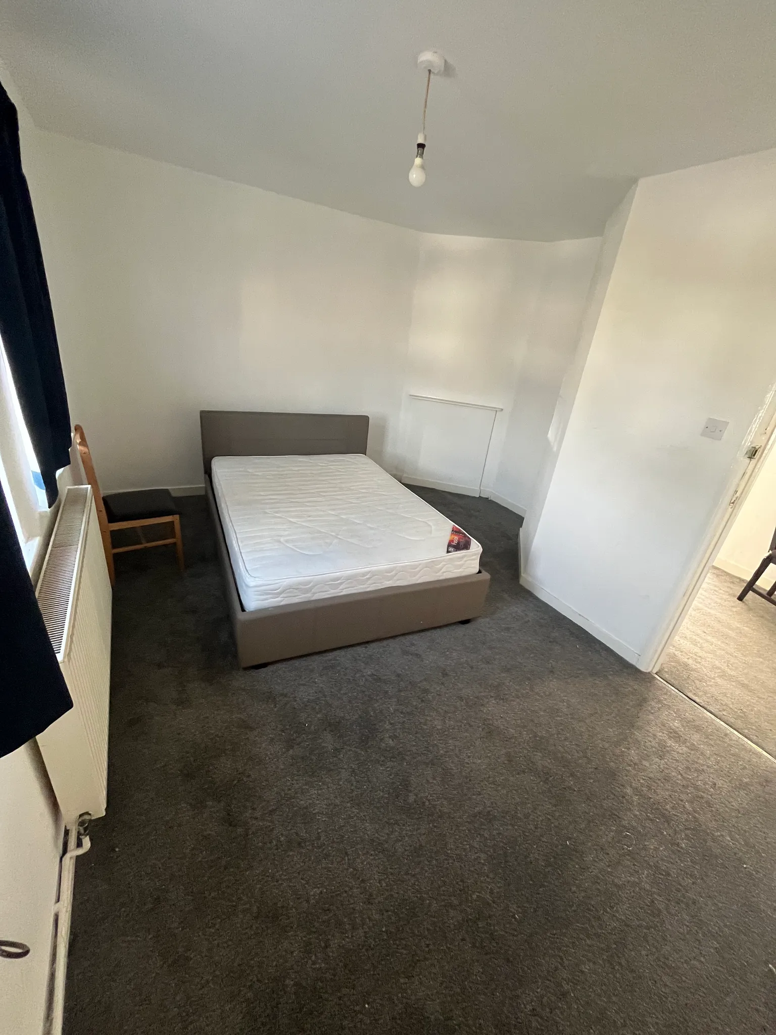 Bedroom with a single bed and mattress, window with dark curtain, radiator and a chair