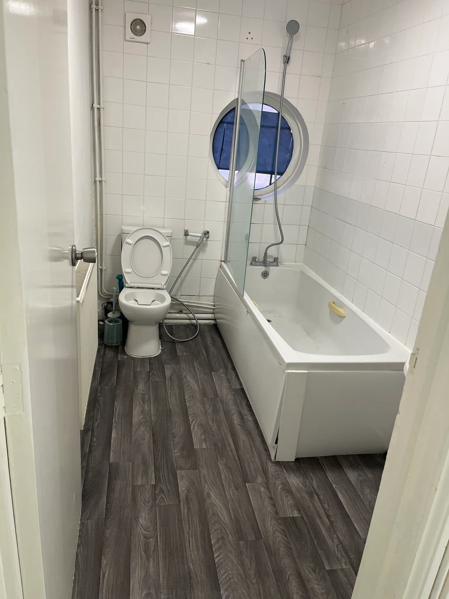Bathroom with a toilet, bathtub with shower head and a round window above the tub