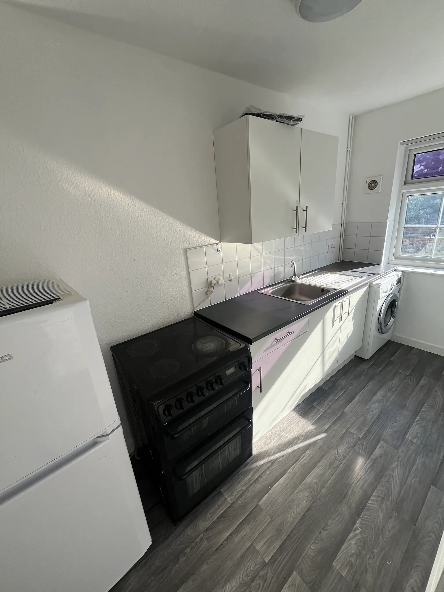 Kitchen with countertop, sink, wall cabinets, freestanding stove, refrigerator and washing machine by a window.